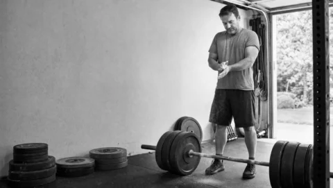 A man chalks his hands beside a loaded barbell in a garage gym